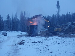 Heavy machinery dumps debris into the air curtain incinerator which is burning the debris.