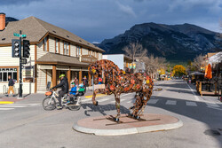 People walk and bike past a metal horse sculpture public art piece by Cedar Mueller on Canmore's Main Street during autumn.
