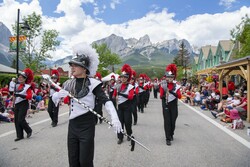 A marching band leader with a baton leads a marching band on Main Street in Canmore